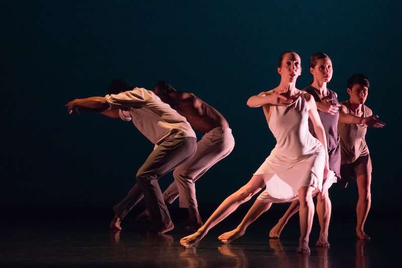 Three women in rose and maeve dresses face the audience while two men create circular shapes with their arms with their backs curved forward